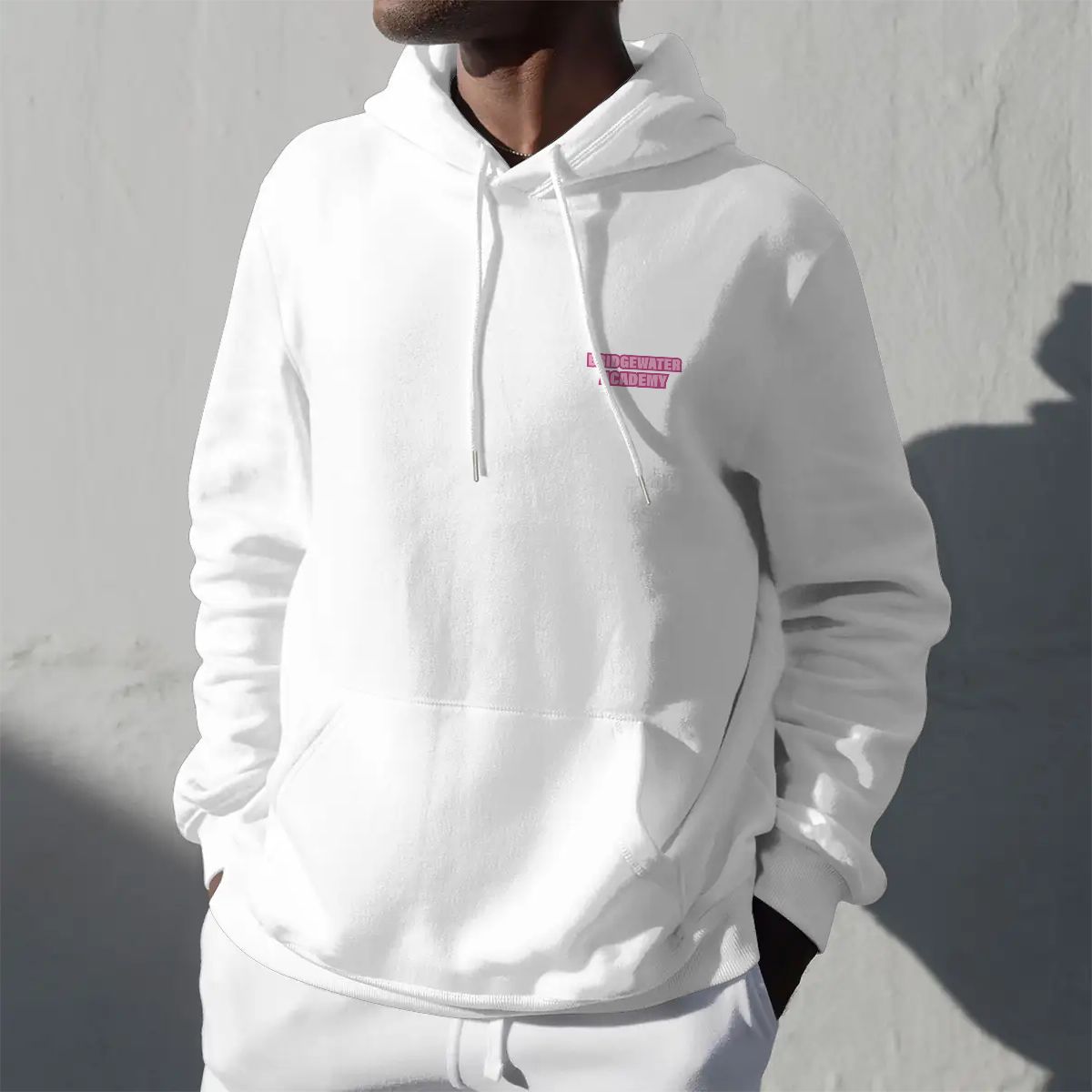 White hoodie with a pink logo worn by a person against a light gray background