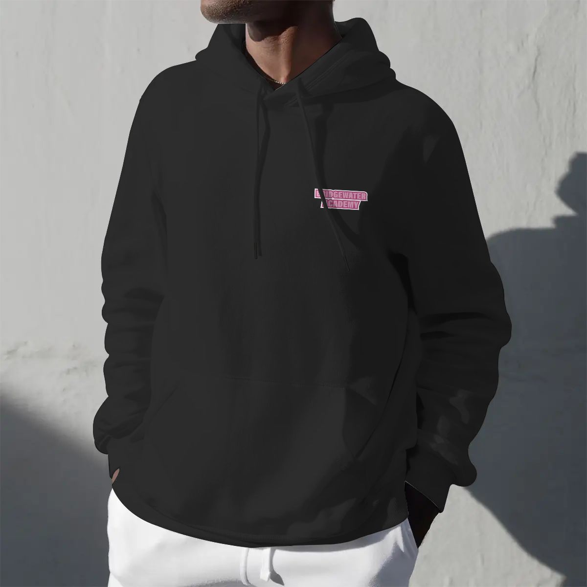 Person wearing a black hoodie with a pink logo against a gray wall